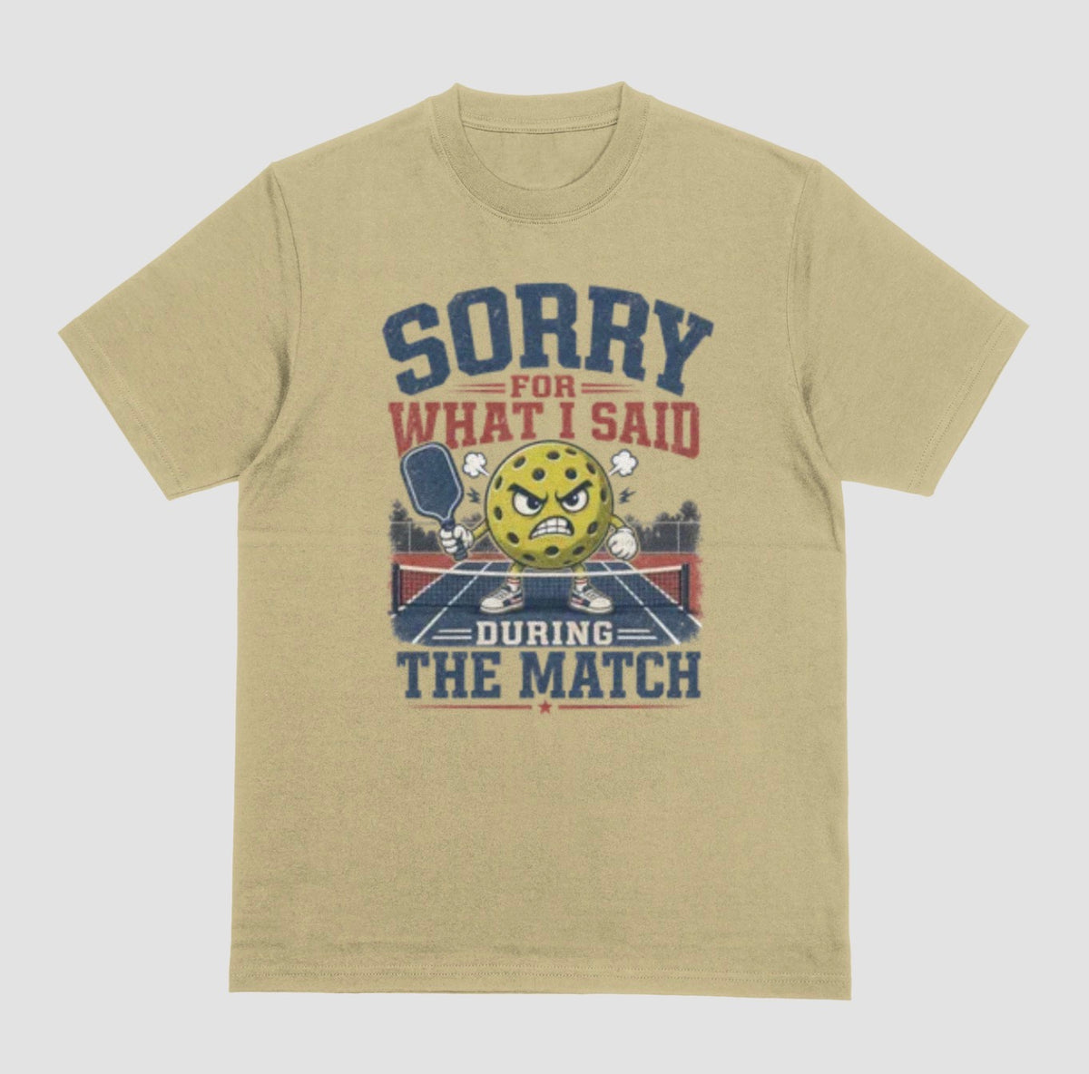 A sand color short-sleeve t-shirt with a distressed graphic on the front. The graphic features a yellow cartoon pickleball with an angry face, a pickleball paddle, and the text 'SORRY FOR WHAT I SAID DURING THE MATCH' in navy blue and red lettering, set against a solid light gray background.