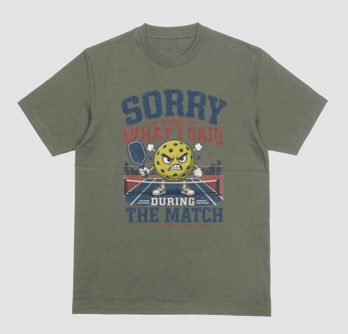 A military green short-sleeve t-shirt with a distressed graphic on the front. The graphic features a yellow cartoon pickleball with an angry face, a pickleball paddle, and the text 'SORRY FOR WHAT I SAID DURING THE MATCH' in navy blue and red lettering, set against a solid light gray background.