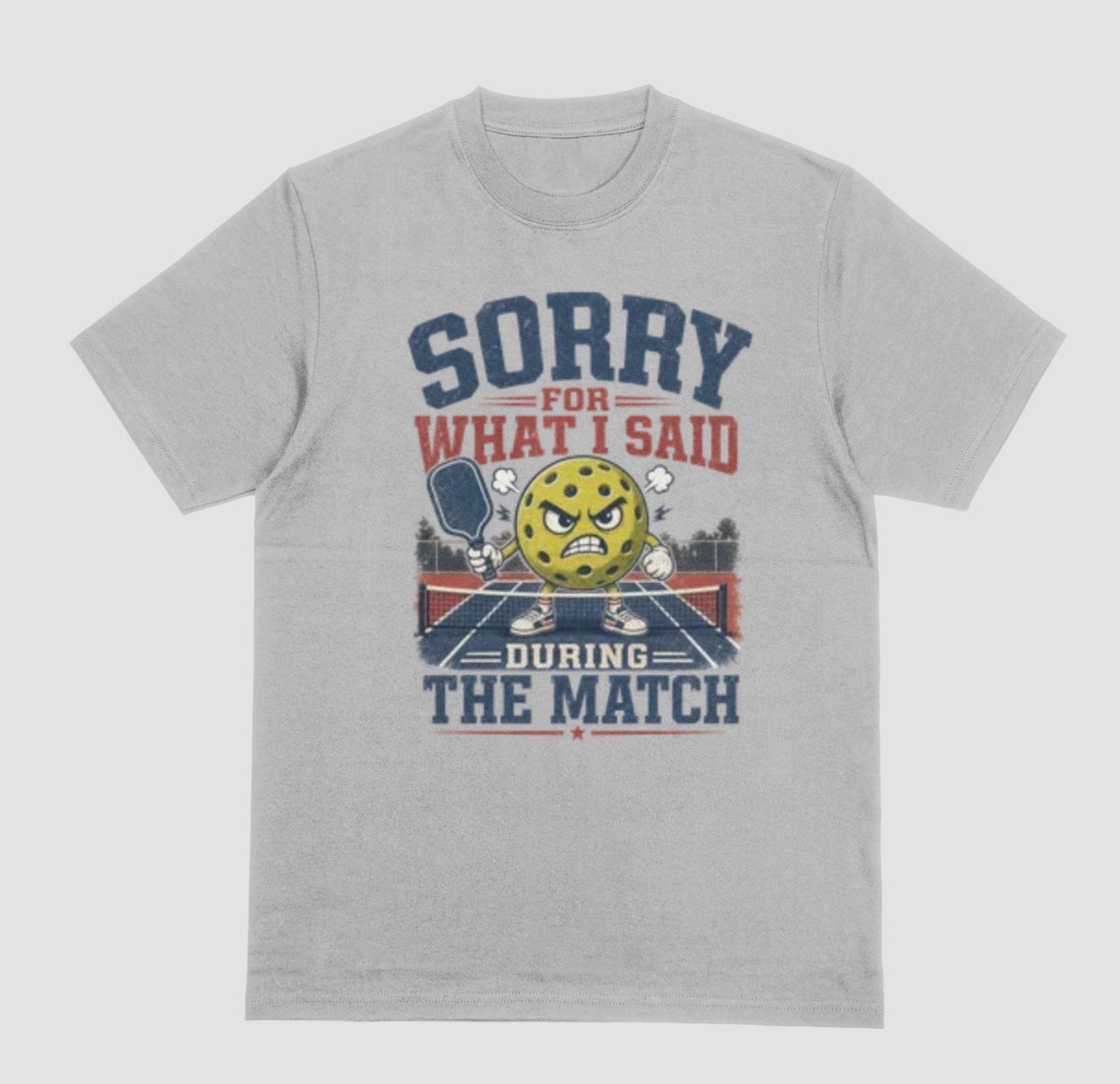 A gray short-sleeve t-shirt with a distressed graphic on the front. The graphic features a yellow cartoon pickleball with an angry face, a pickleball paddle, and the text 'SORRY FOR WHAT I SAID DURING THE MATCH' in navy blue and red lettering, set against a solid light gray background.