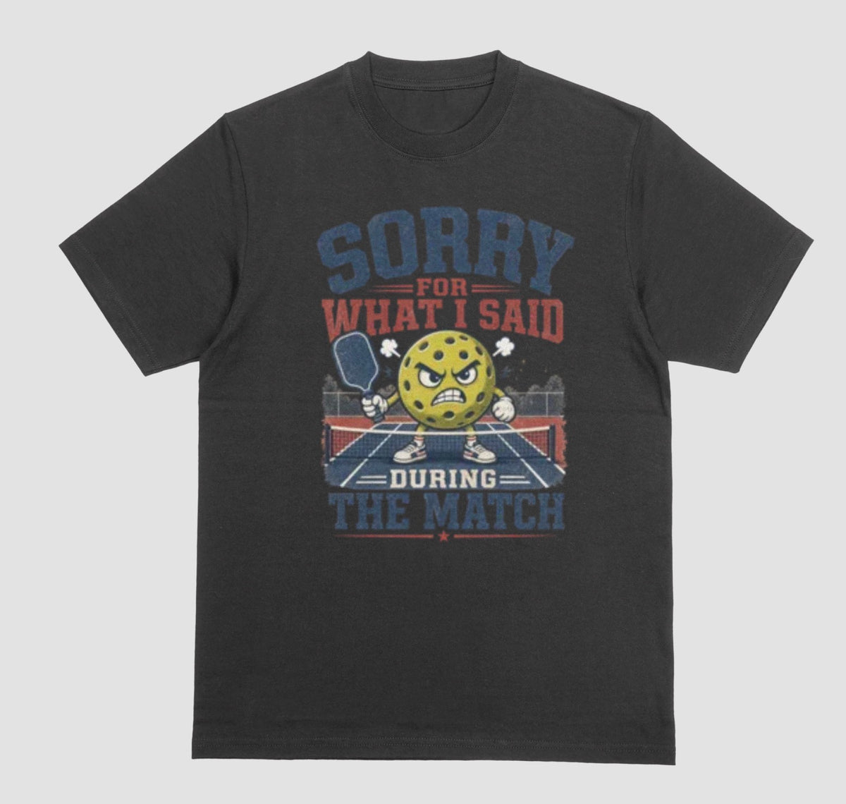 A black short-sleeve t-shirt with a distressed graphic on the front. The graphic features a yellow cartoon pickleball with an angry face, a pickleball paddle, and the text 'SORRY FOR WHAT I SAID DURING THE MATCH' in navy blue and red lettering, set against a solid light gray background.