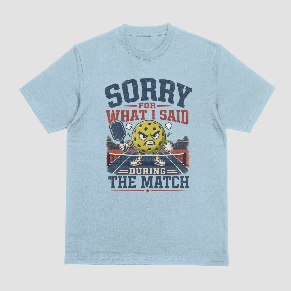 A light blue short-sleeve t-shirt with a distressed graphic on the front. The graphic features a yellow cartoon pickleball with an angry face, a pickleball paddle, and the text 'SORRY FOR WHAT I SAID DURING THE MATCH' in navy blue and red lettering, set against a solid light gray background.