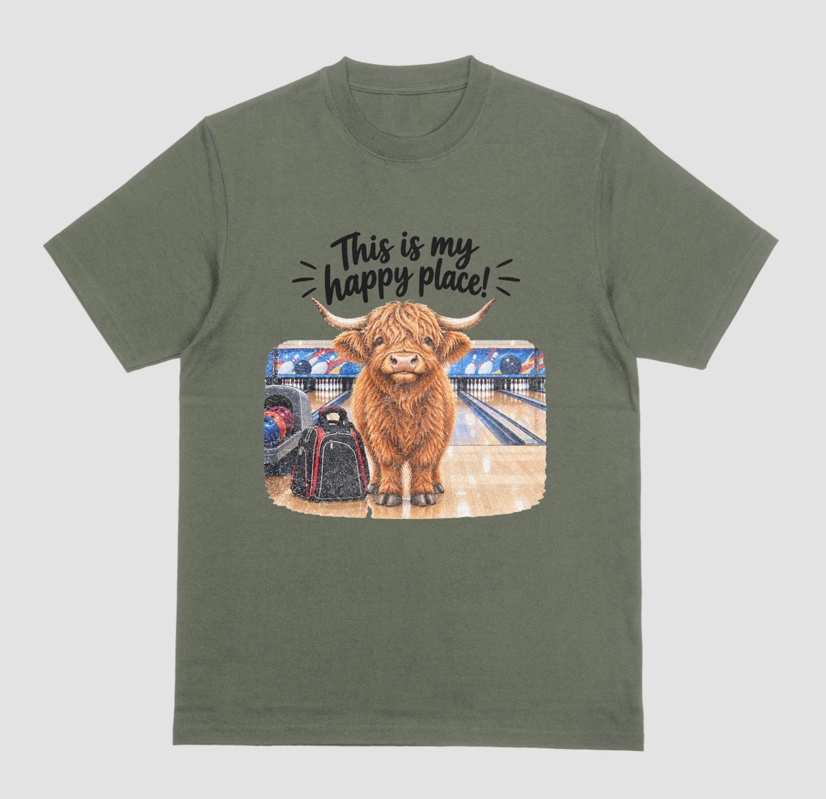 A military green short-sleeve crewneck t-shirt featuring a graphic of a Highland cow standing on a bowling lane with the text 'This is my happy place!' above it, displayed on a bowling alley background.