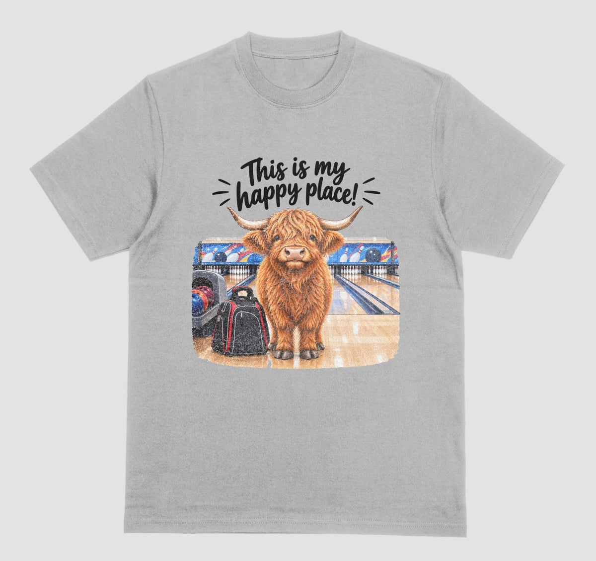 A light gray short-sleeve crewneck t-shirt featuring a graphic of a Highland cow standing on a bowling lane with the text 'This is my happy place!' above it, displayed on a bowling alley background.