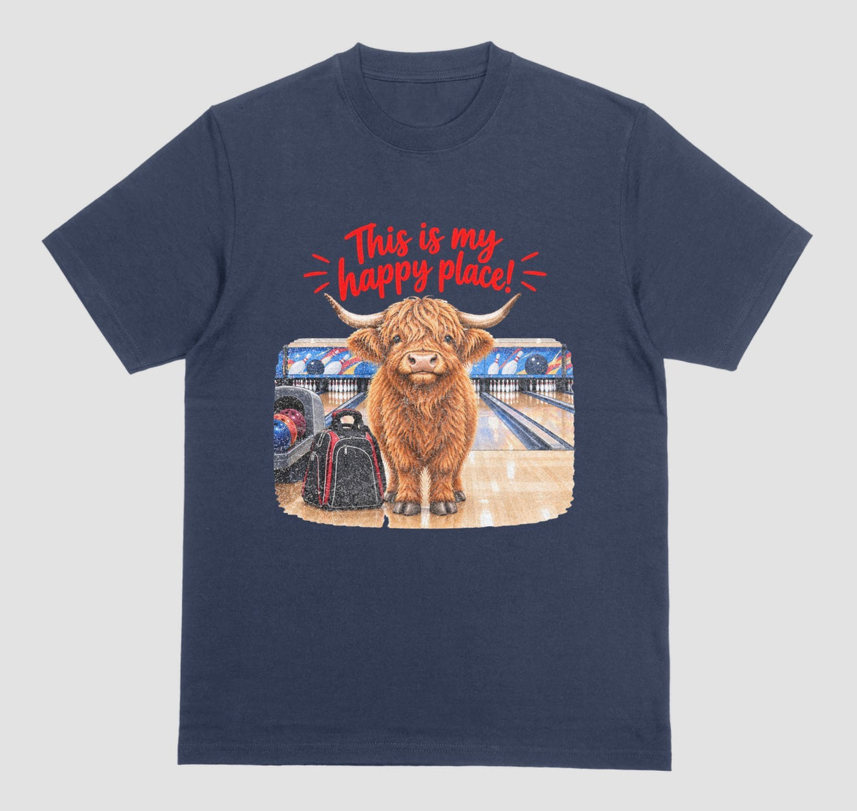 A navy blue short-sleeve crewneck t-shirt featuring a graphic of a Highland cow standing on a bowling lane with the text 'This is my happy place!' above it, displayed on a bowling alley background.