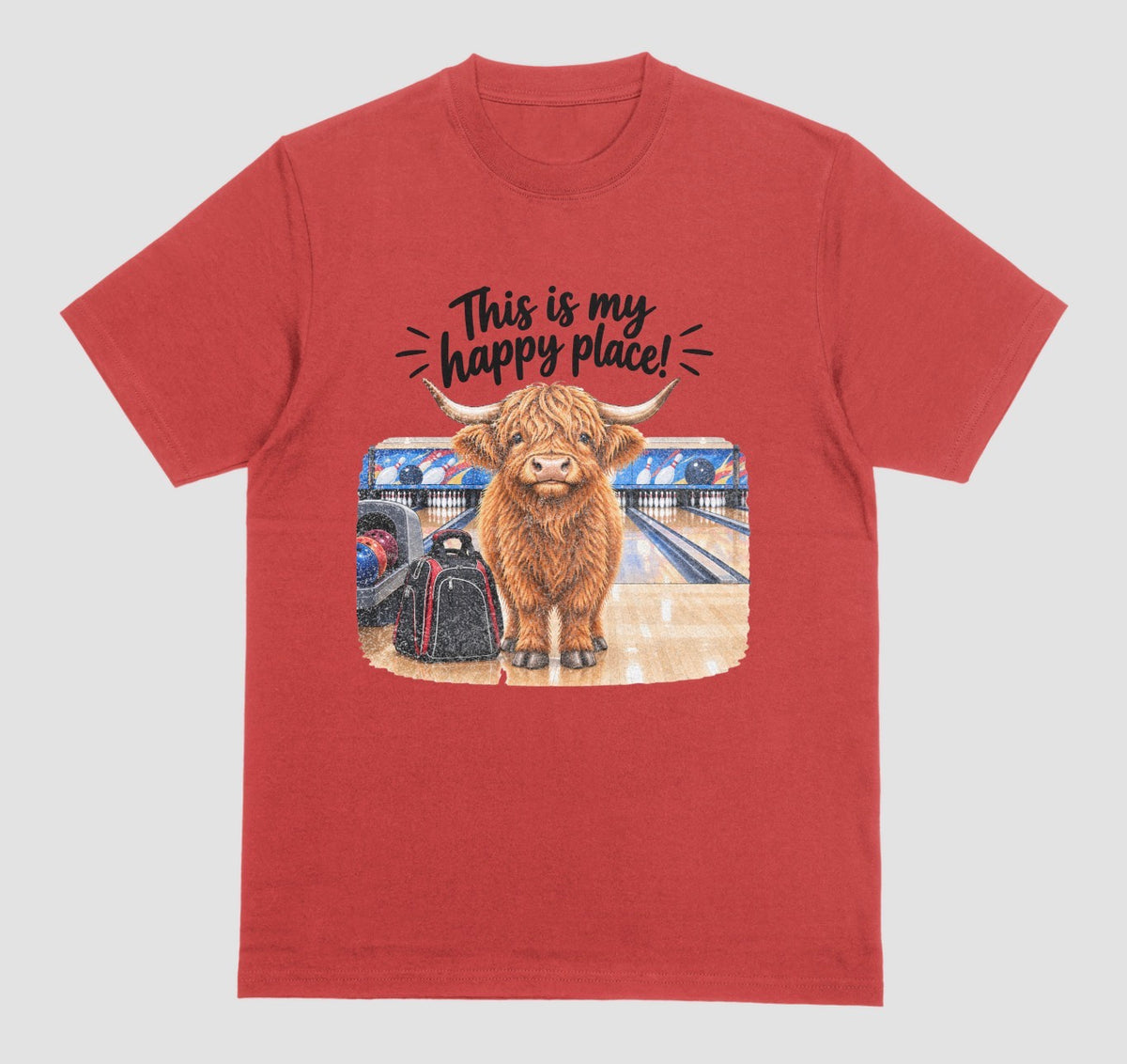 A red short-sleeve crewneck t-shirt featuring a graphic of a Highland cow standing on a bowling lane with the text 'This is my happy place!' above it, displayed on a bowling alley background.