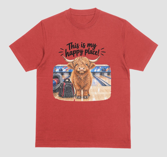 A red short-sleeve crewneck t-shirt featuring a graphic of a Highland cow standing on a bowling lane with the text 'This is my happy place!' above it, displayed on a bowling alley background.