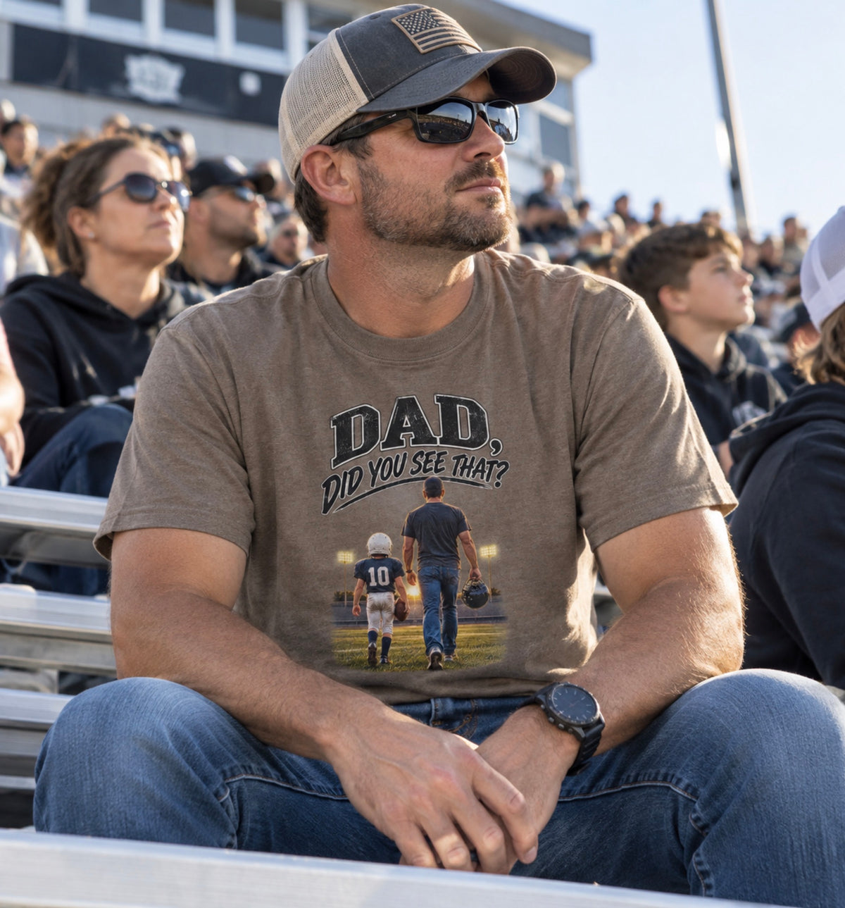 A man sitting in stadium bleachers wearing a brown savana The graphic shows a father and son walking on a football field at night, with the text 'DAD DID YOU SEE THAT?' above them.