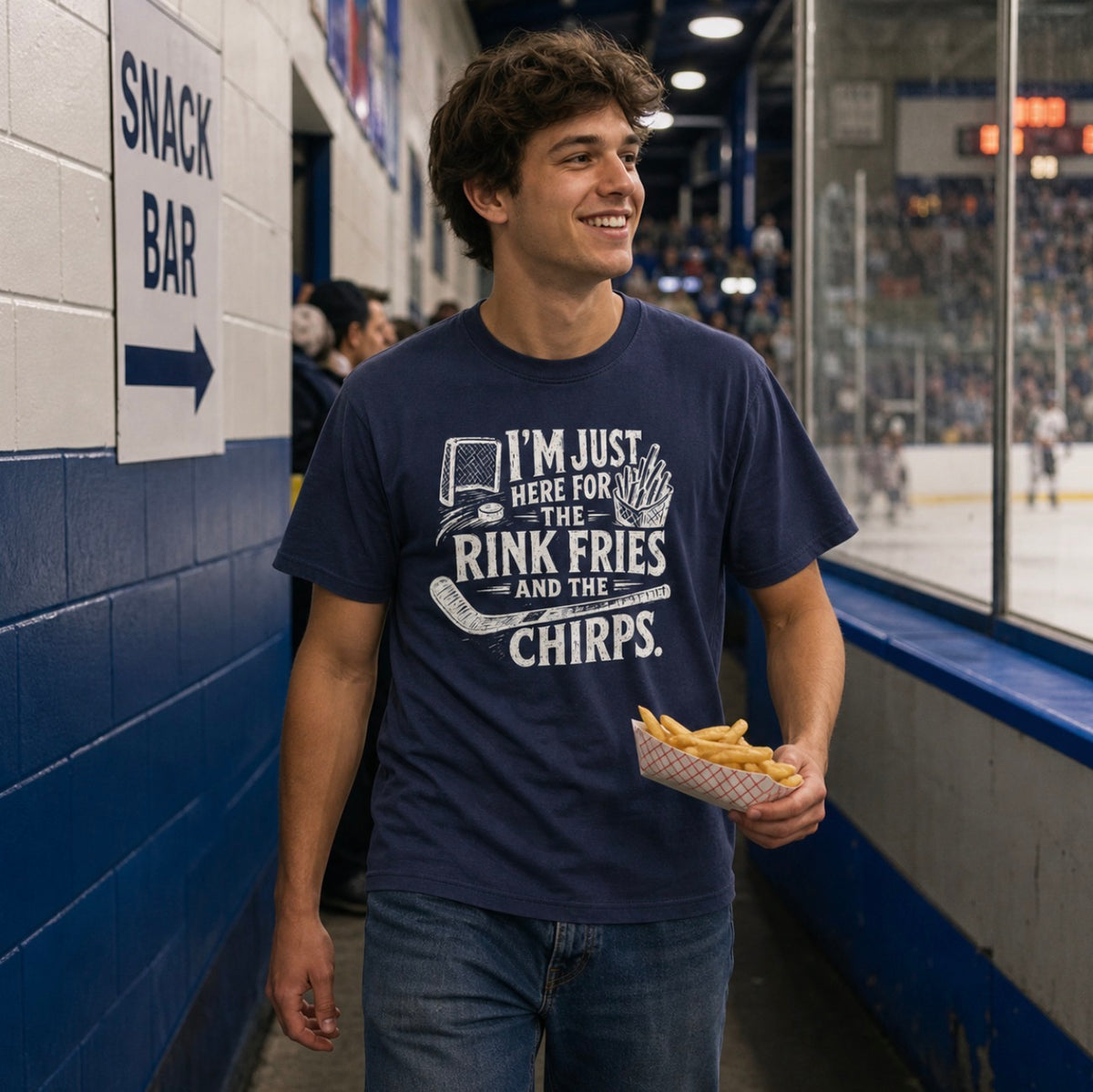 A man wearing a navy blue t-shirt with white distressed hockey graphic reading “I’m just here for the rink fries and the chirps” with a hockey net, puck, stick, and fries at a hockey game walking back from the snack bar with fries
