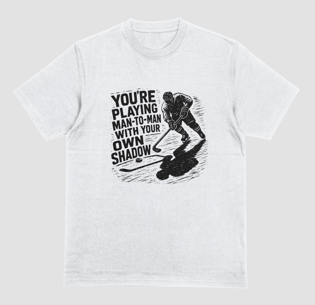 A white hockey t-shirt with black graphic of a skater and his long shadow, reading “You’re playing man-to-man with your own shadow”