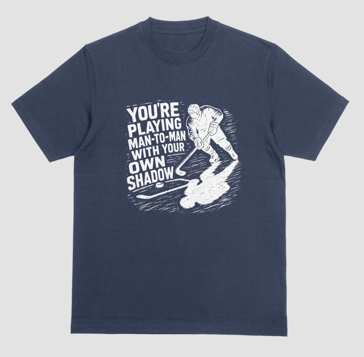 A navy blue hockey t-shirt with white graphic of a skater and his long shadow, reading “You’re playing man-to-man with your own shadow”