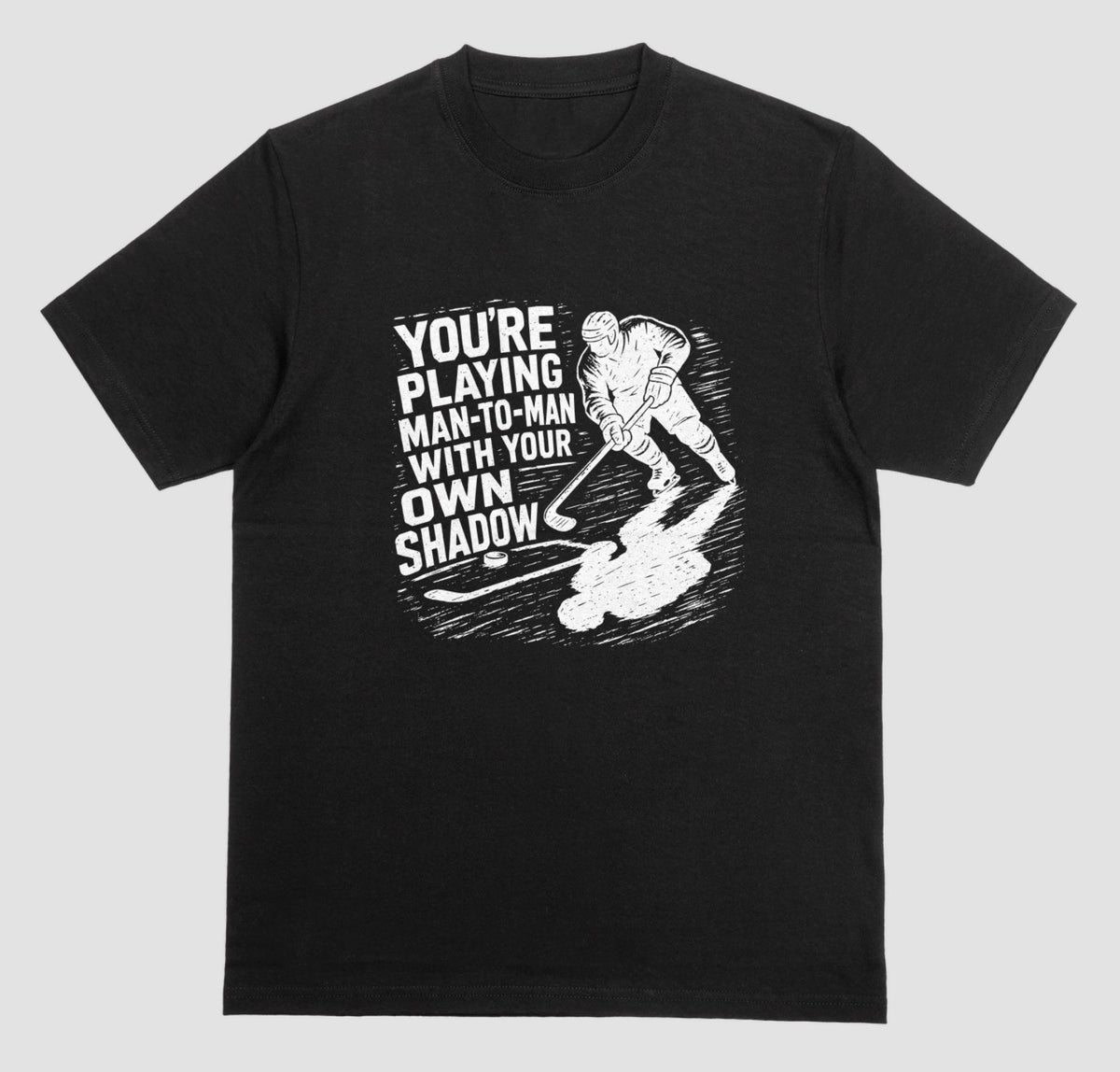 A black hockey t-shirt with white graphic of a skater and his long shadow, reading “You’re playing man-to-man with your own shadow”