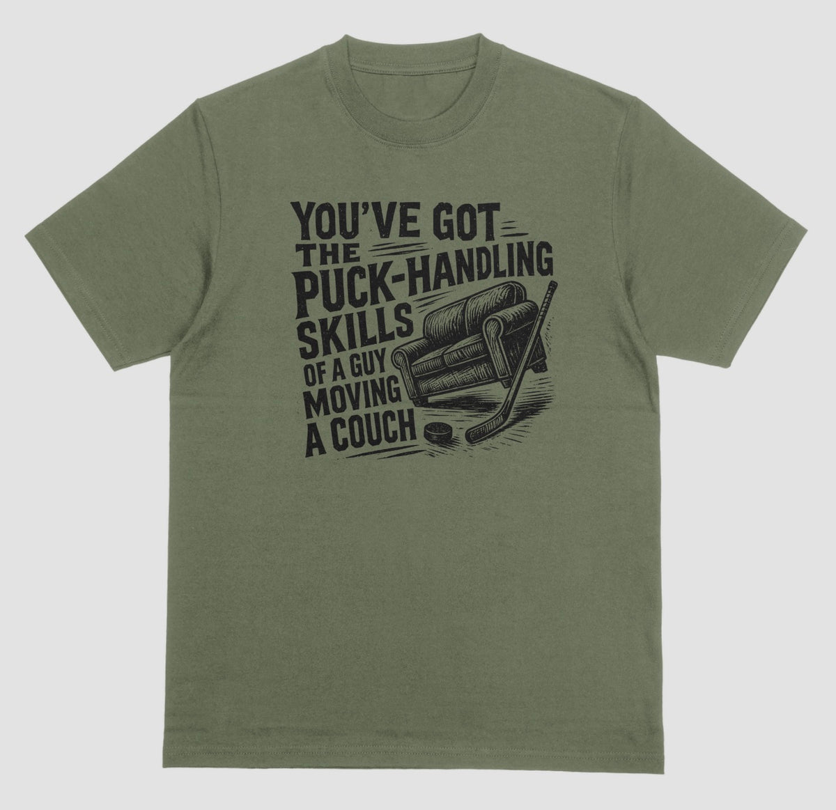 A military green hockey humor t-shirt with black graphic of a couch, hockey stick, and puck, reading “You’ve got the puck-handling skills of a guy moving a couch”