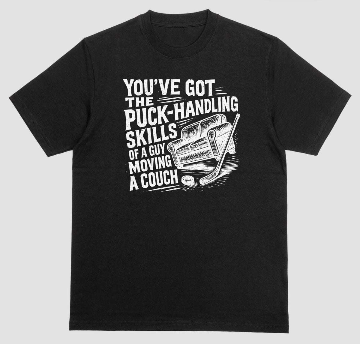 A black hockey humor t-shirt with white graphic of a couch, hockey stick, and puck, reading “You’ve got the puck-handling skills of a guy moving a couch”