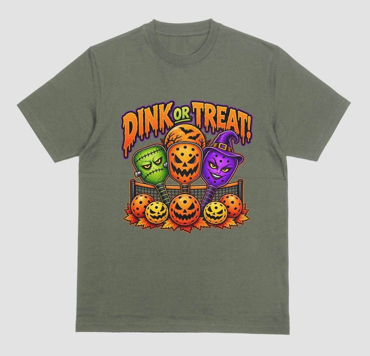 A military green t-shirt with “Dink or Treat!” Halloween design of three spooky pickleball paddles and jack-o’-lantern pickleballs