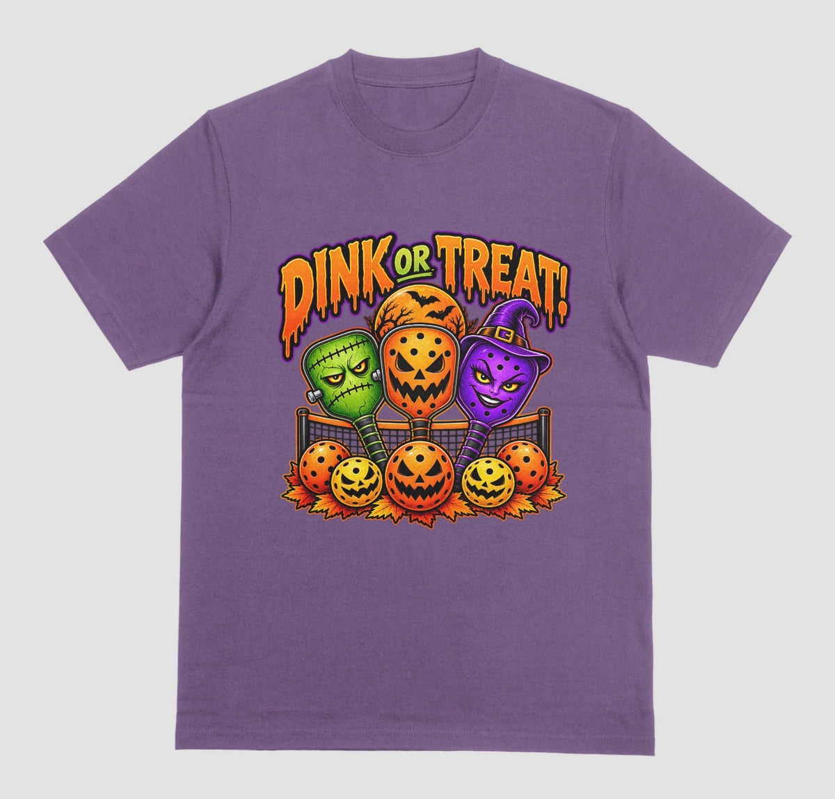 A purple t-shirt with “Dink or Treat!” Halloween design of three spooky pickleball paddles and jack-o’-lantern pickleballs