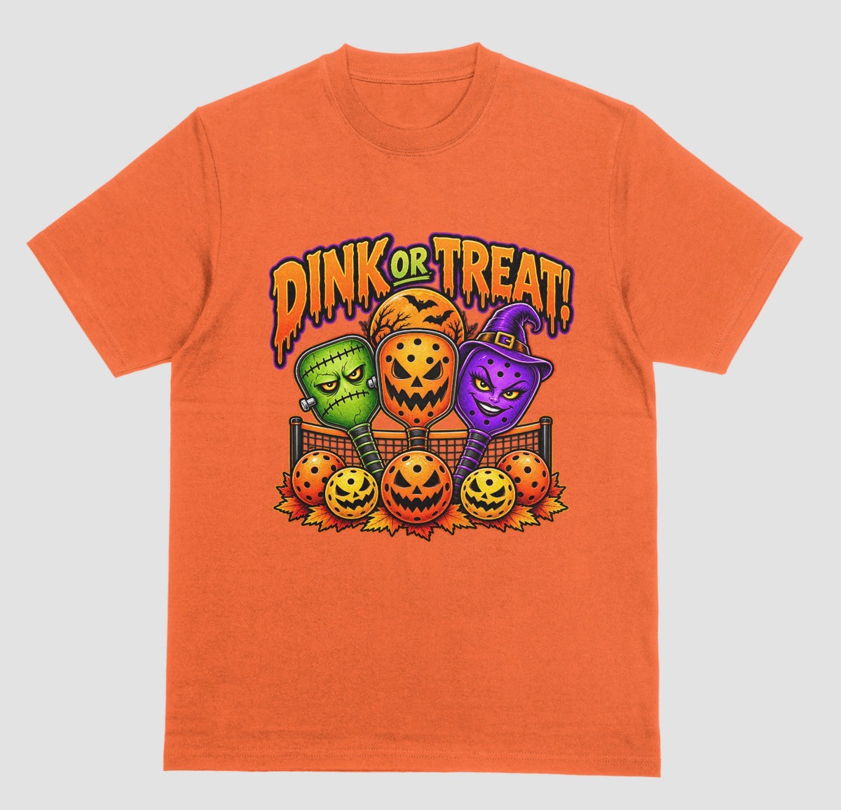 An orange t-shirt with “Dink or Treat!” Halloween design of three spooky pickleball paddles and jack-o’-lantern pickleballs
