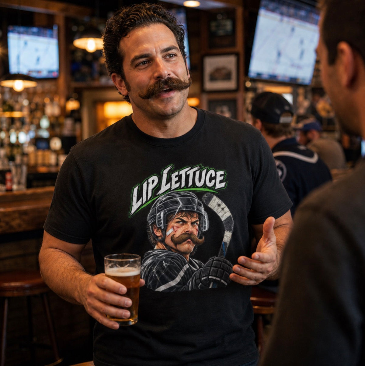 Man with a handlebar mustache wearing black t-shirt with “Lip Lettuce” in white and green lettering above a mustached hockey player illustration, holding a beer at a bar