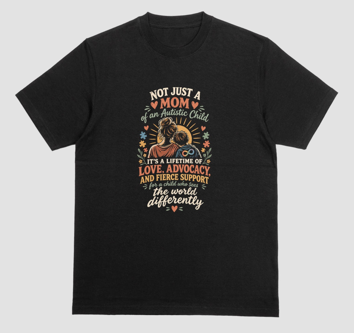 A black t-shirt with a retro-style graphic of a mother holding her child and the text ‘Not Just a Mom of an Autistic Child. It’s a lifetime of love, advocacy, and fierce support for a child who sees the world differently.’