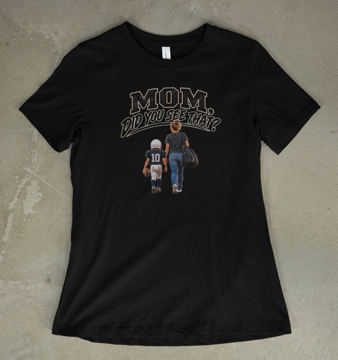A black short-sleeve t-shirt with a graphic print on the front that reads 'MOM DID YOU SEE THAT?' above an illustration of a mother and child walking away, laid flat on a textured concrete surface.