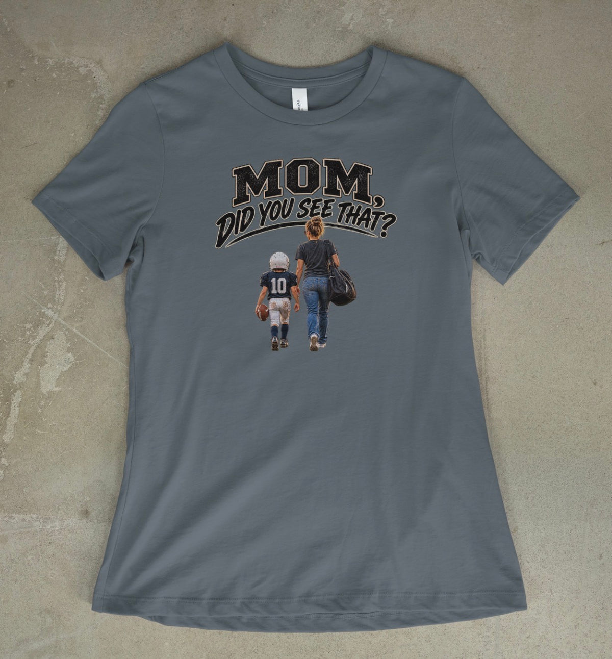 A vintage denim short-sleeve t-shirt with a graphic print on the front that reads 'MOM DID YOU SEE THAT?' above an illustration of a mother and child walking away, laid flat on a textured concrete surface.