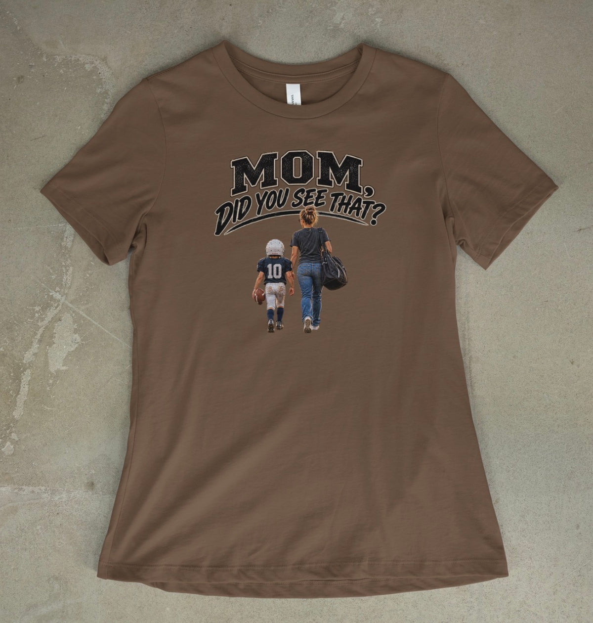 A vintage brown short-sleeve t-shirt with a graphic print on the front that reads 'MOM DID YOU SEE THAT?' above an illustration of a mother and child walking away, laid flat on a textured concrete surface.