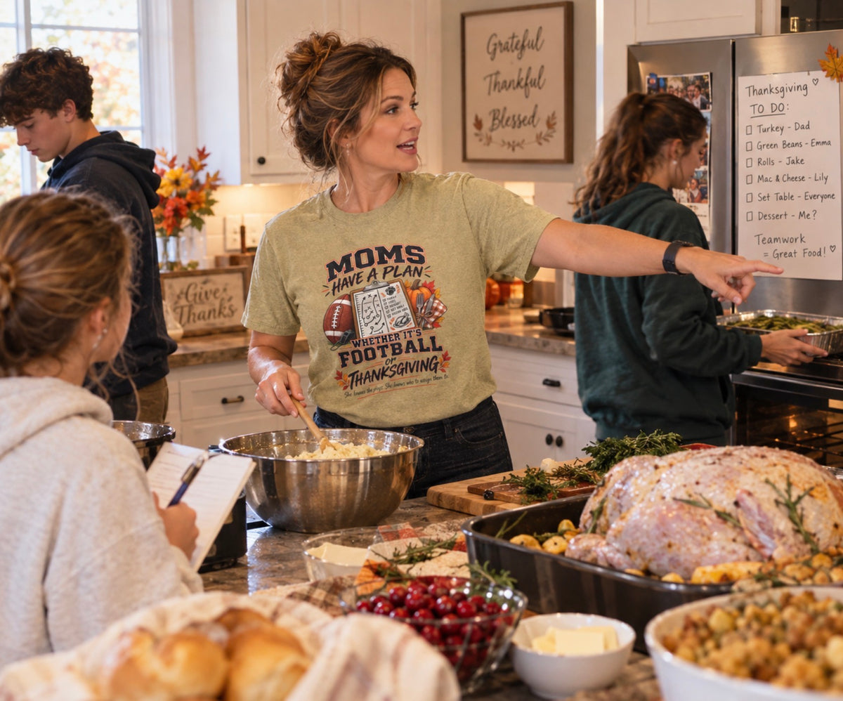 Woman wearing sand 'Moms Have a Plan' football and Thanksgiving graphic t-shirt while cooking Thanksgiving dinner and delegating assignments