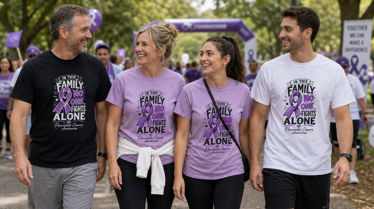 Four people walking outdoors at Pancreatic awareness event, wearing shirts with a purple ribbon graphic and the text 'In This Family NO ONE Fights Alone' Two shirts are lilac and one is white; a man on the left wears a black shirt.