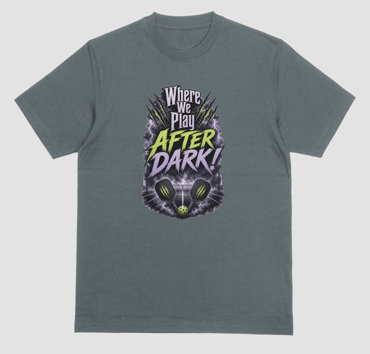 A dark heather t-shirt with a spooky pickleball graphic reading 'Where We Play After Dark!' showing two crossed paddles and a ball on a court inside a lightning-filled storm cloud.