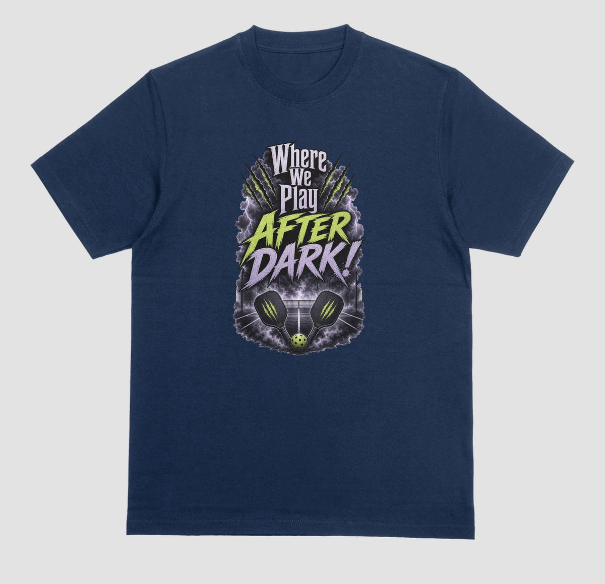 A midnight t-shirt with a spooky pickleball graphic reading 'Where We Play After Dark!' showing two crossed paddles and a ball on a court inside a lightning-filled storm cloud.