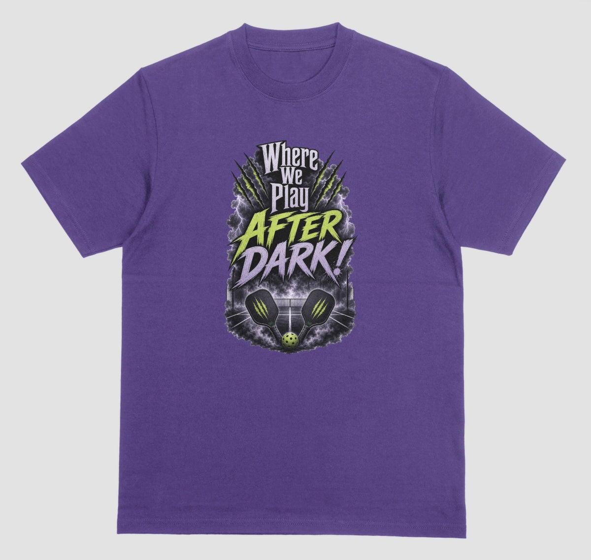 A purple t-shirt with a spooky pickleball graphic reading 'Where We Play After Dark!' showing two crossed paddles and a ball on a court inside a lightning-filled storm cloud.