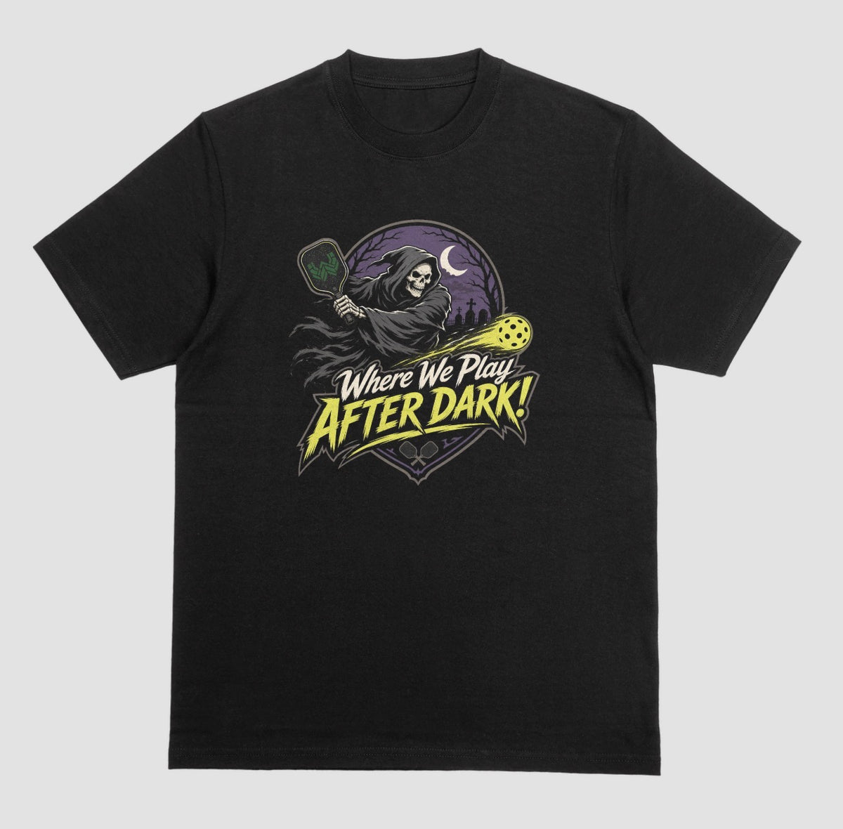 A black t-shirt with a spooky pickleball graphic reading 'Where We Play After Dark!' showing a hooded grim reaper swinging a paddle at a glowing yellow ball.