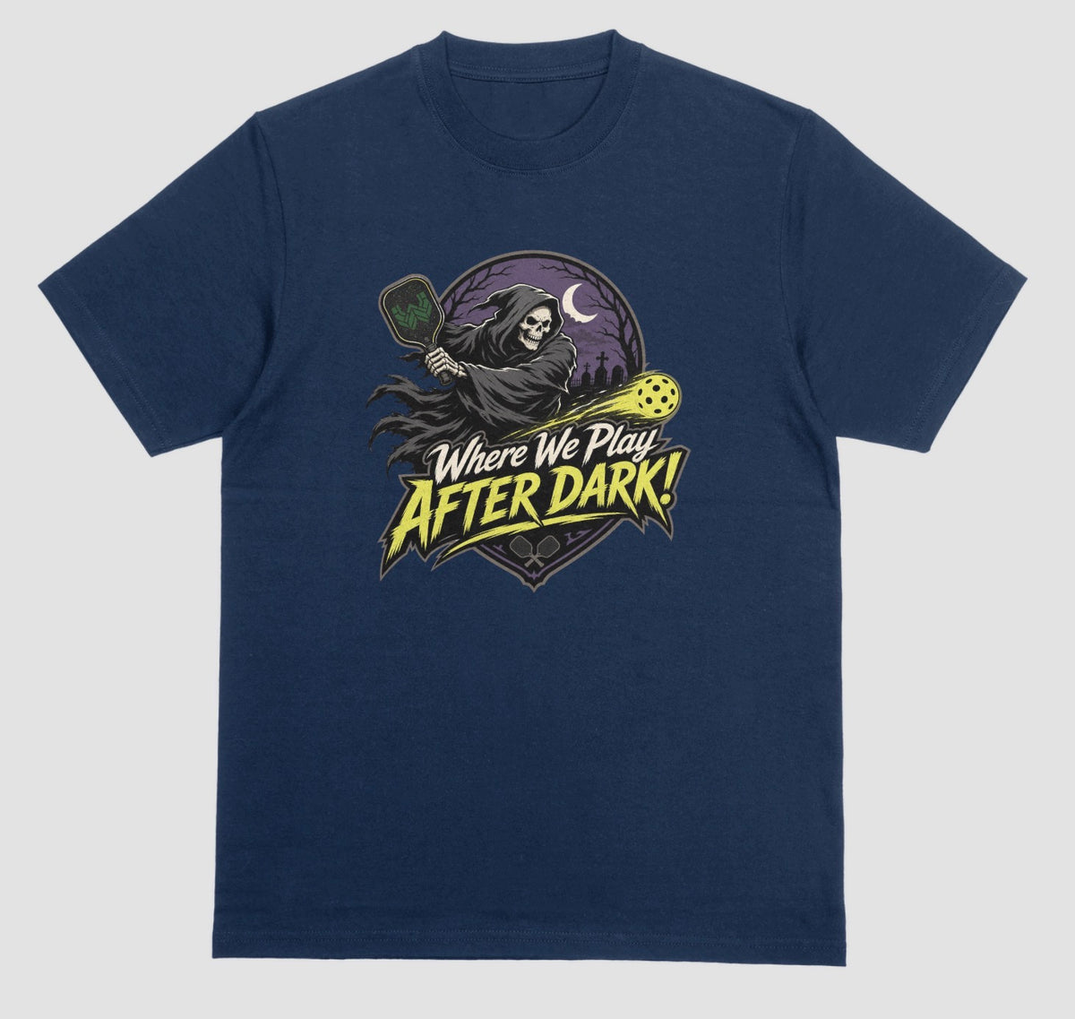A midnight t-shirt with a spooky pickleball graphic reading 'Where We Play After Dark!' showing a hooded grim reaper swinging a paddle at a glowing yellow ball.