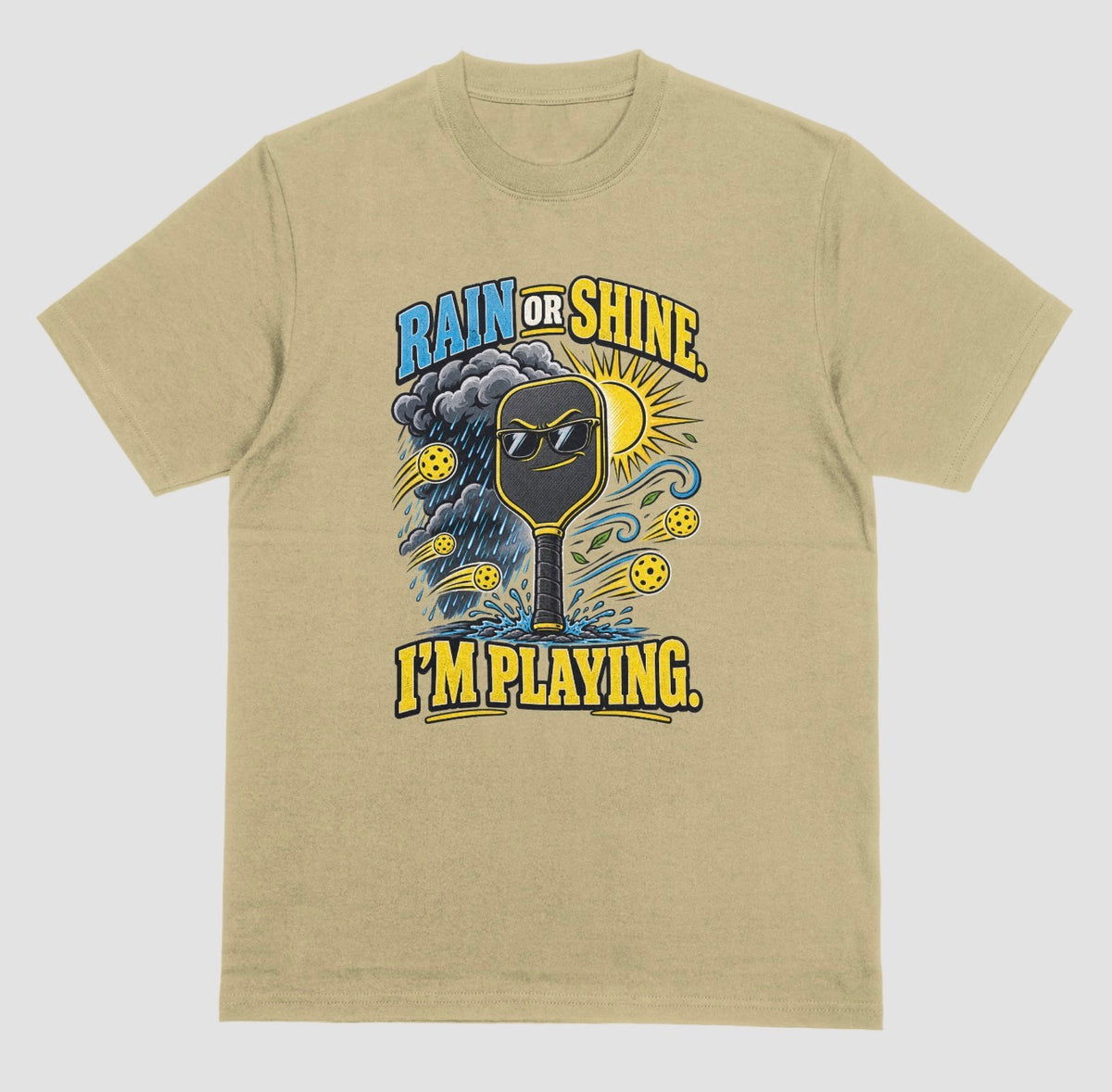 A sand color Funny pickleball shirt with a sunglasses paddle, storm cloud and sun that says Rain or Shine, I’m Playing