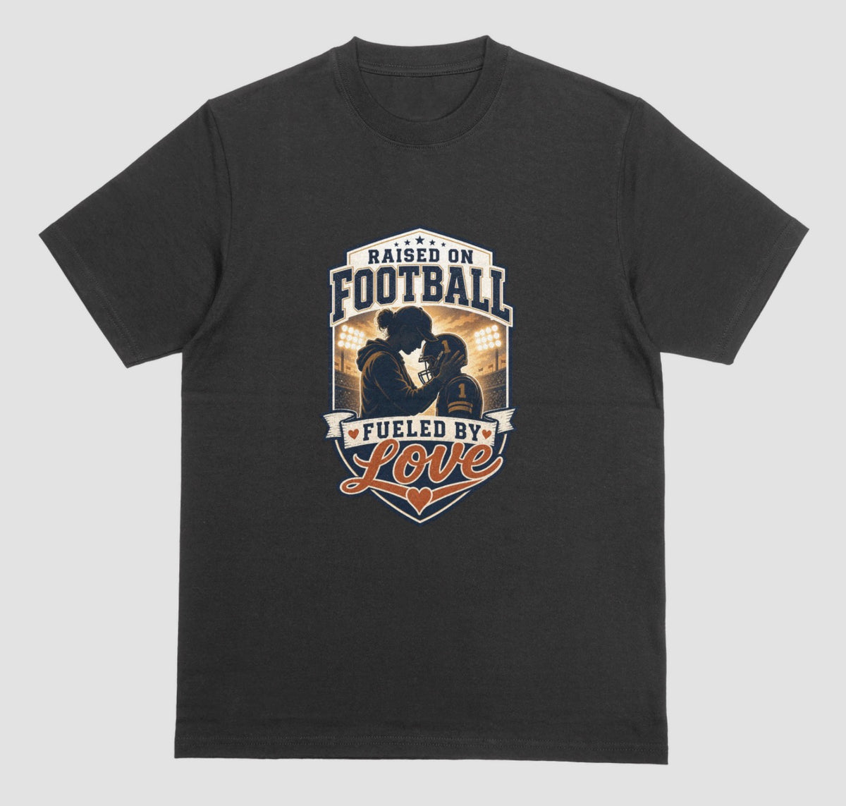 A black crewneck t-shirt with a vintage-style football graphic on the chest. The graphic features a silhouette of a football player with the text 'RAISED ON FOOTBALL' and 'FUELED BY Love' in navy, white, and orange.