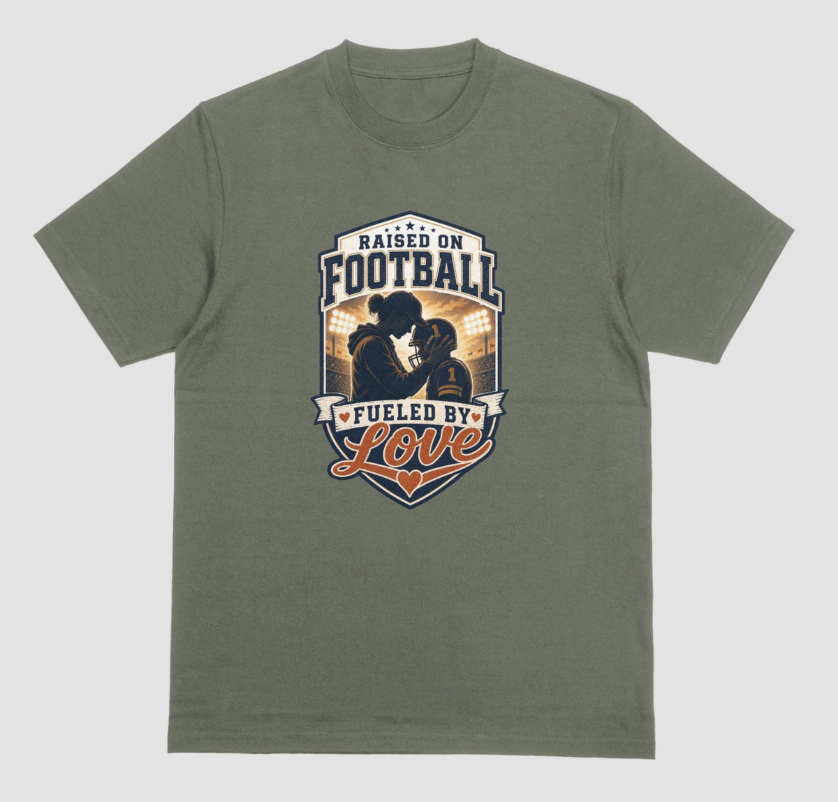 A military green crewneck t-shirt with a vintage-style football graphic on the chest. The graphic features a silhouette of a football player with the text 'RAISED ON FOOTBALL' and 'FUELED BY Love' in navy, white, and orange.