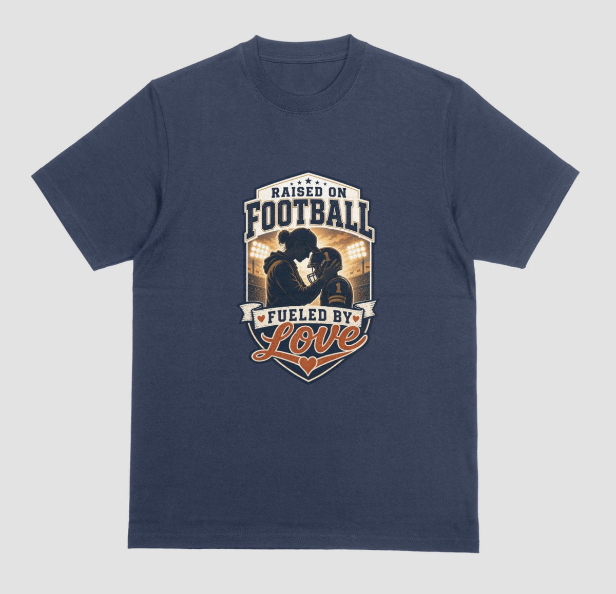 A navy blue crewneck t-shirt with a vintage-style football graphic on the chest. The graphic features a silhouette of a football player with the text 'RAISED ON FOOTBALL' and 'FUELED BY Love' in navy, white, and orange.