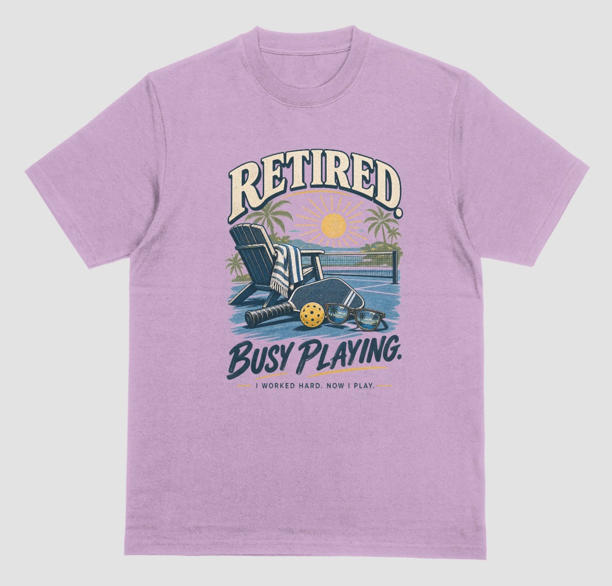 A heather radiant orchid short-sleeve t-shirt with a retro graphic on the chest. The graphic features the words short-sleeve t-shirt with a retro graphic on the chest. The graphic features the words Retired pickleball shirt in sand with a beach chair and paddle design that says Retired, Busy Playing, I Worked Hard Now I Play