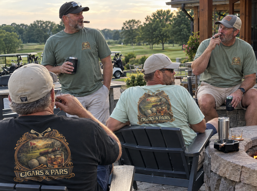 Four men wearing matching green and black Cigars & Pars t-shirts and caps sit and stand on an outdoor patio near a fire pit and golf course in the background.