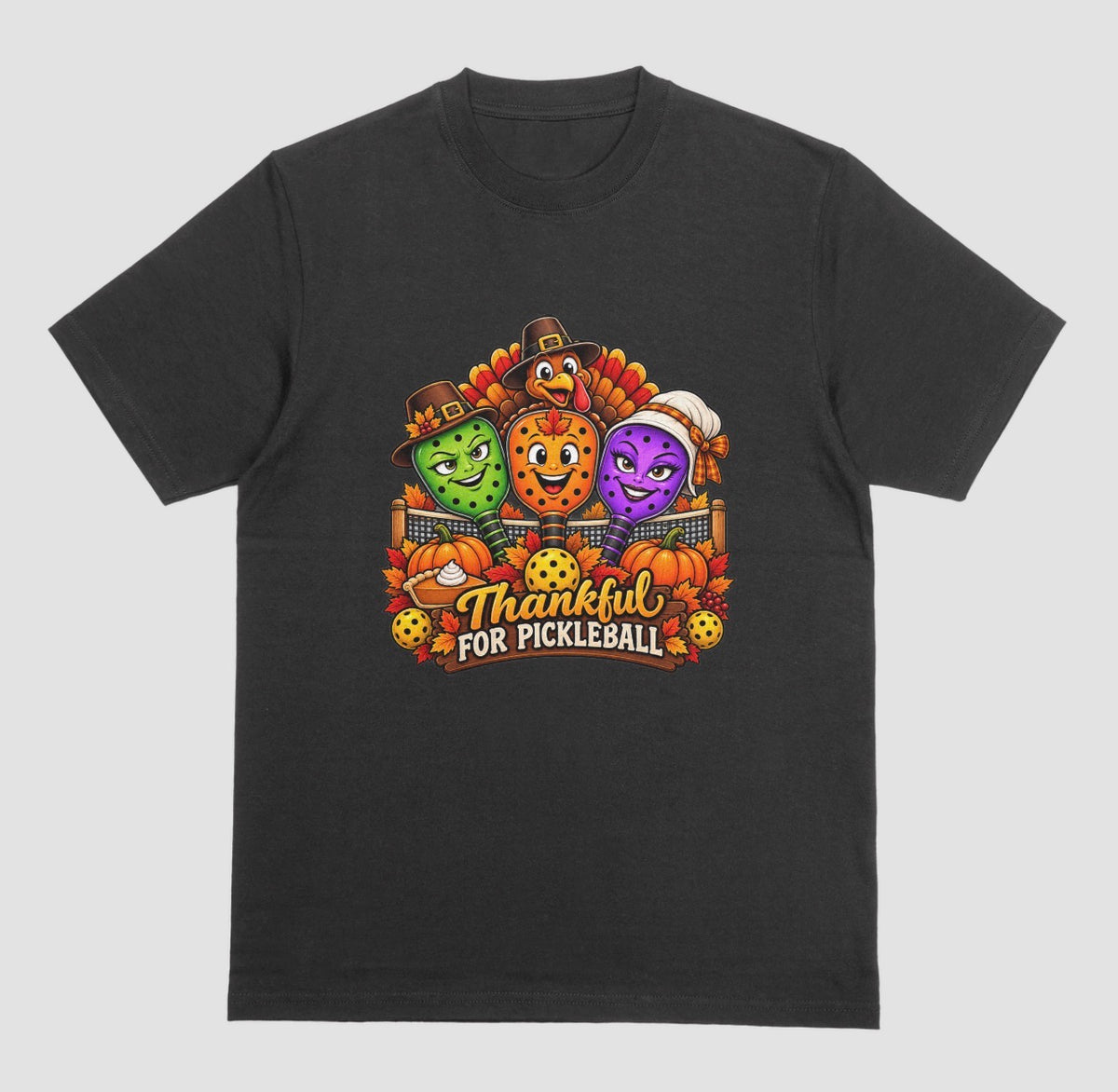A black t-shirt with “Thankful for Pickleball” design of three pilgrim-hat paddles, a turkey, pumpkins, and pie