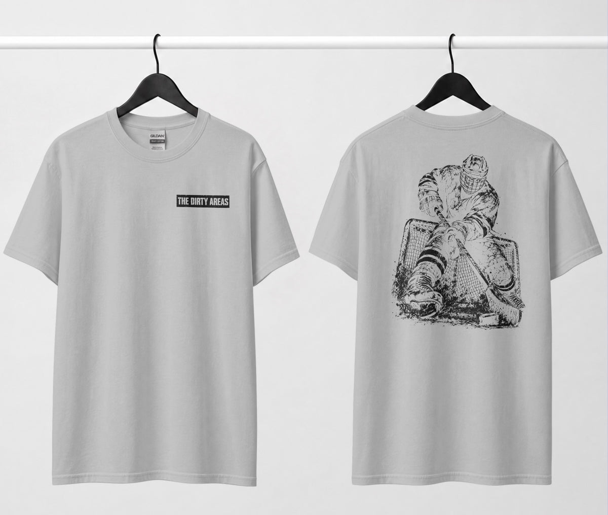 Front and back of a grey t-shirt hanging side by side: the front has a small 'The Dirty Areas' label on the chest, and the back has a large black hockey player battling in front of the net.
