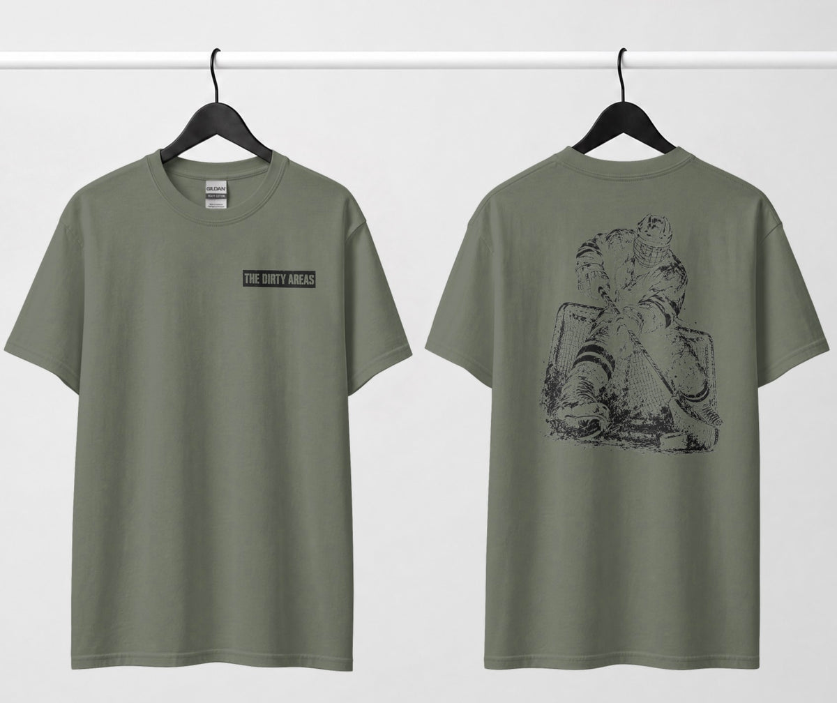Front and back of a Military Green t-shirt hanging side by side: the front has a small 'The Dirty Areas' label on the chest, and the back has a large black hockey player battling in front of the net.