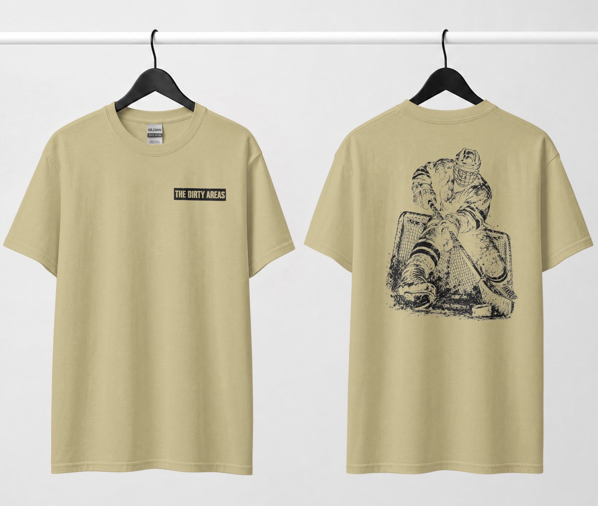 Front and back of a sand color t-shirt hanging side by side: the front has a small 'The Dirty Areas' label on the chest, and the back has a large black hockey player battling in front of the net.
