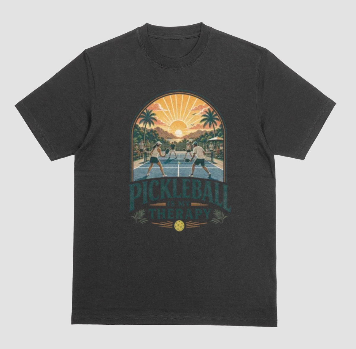 A black crewneck t-shirt featuring a retro-style graphic of pickleball players on a court with a sunset and palm trees, and the text 'PICKLEBALL IS MY THERAPY' printed below.