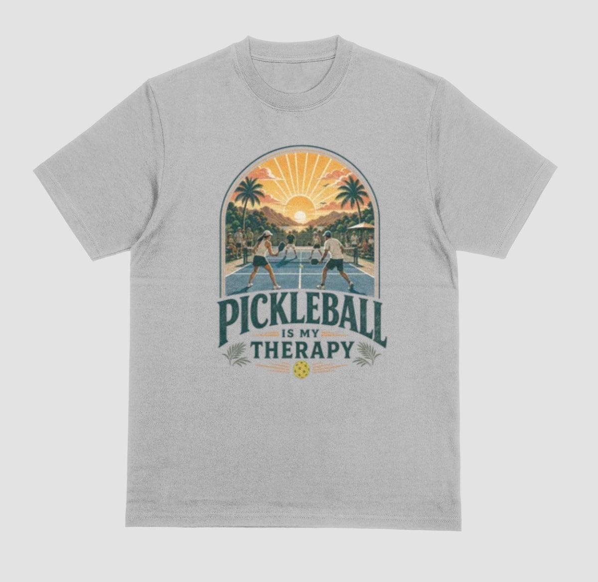 A gray crewneck t-shirt featuring a retro-style graphic of pickleball players on a court with a sunset and palm trees, and the text 'PICKLEBALL IS MY THERAPY' printed below.
