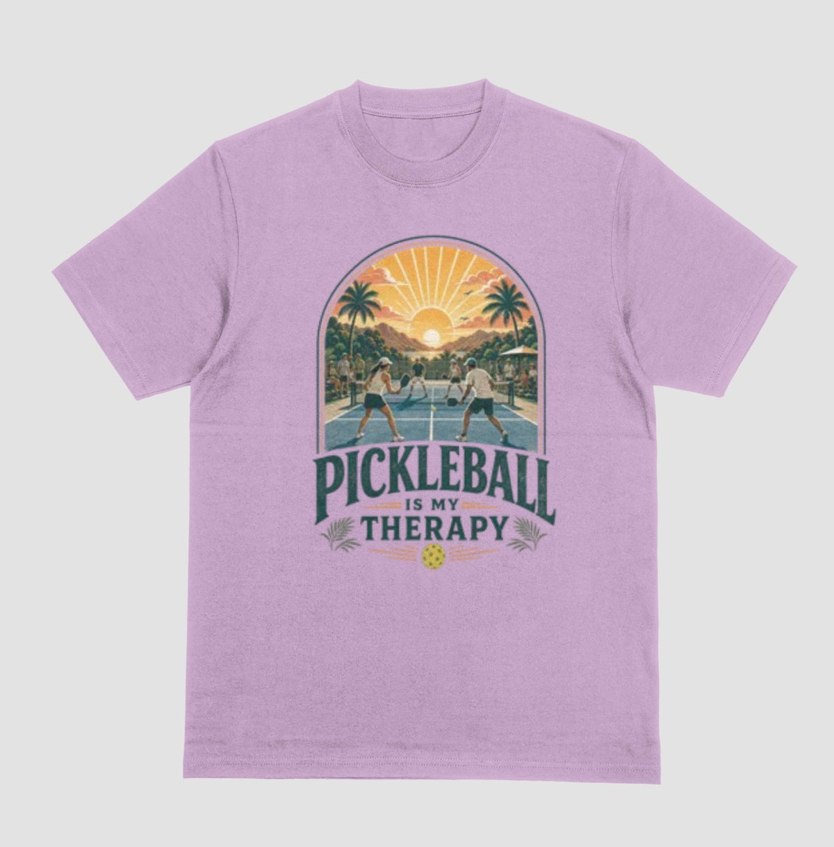 A lilac crewneck t-shirt featuring a retro-style graphic of pickleball players on a court with a sunset and palm trees, and the text 'PICKLEBALL IS MY THERAPY' printed below.