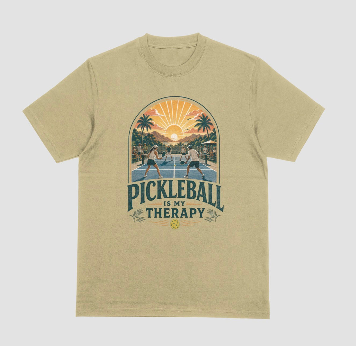 A sand crewneck t-shirt featuring a retro-style graphic of pickleball players on a court with a sunset and palm trees, and the text 'PICKLEBALL IS MY THERAPY' printed below.