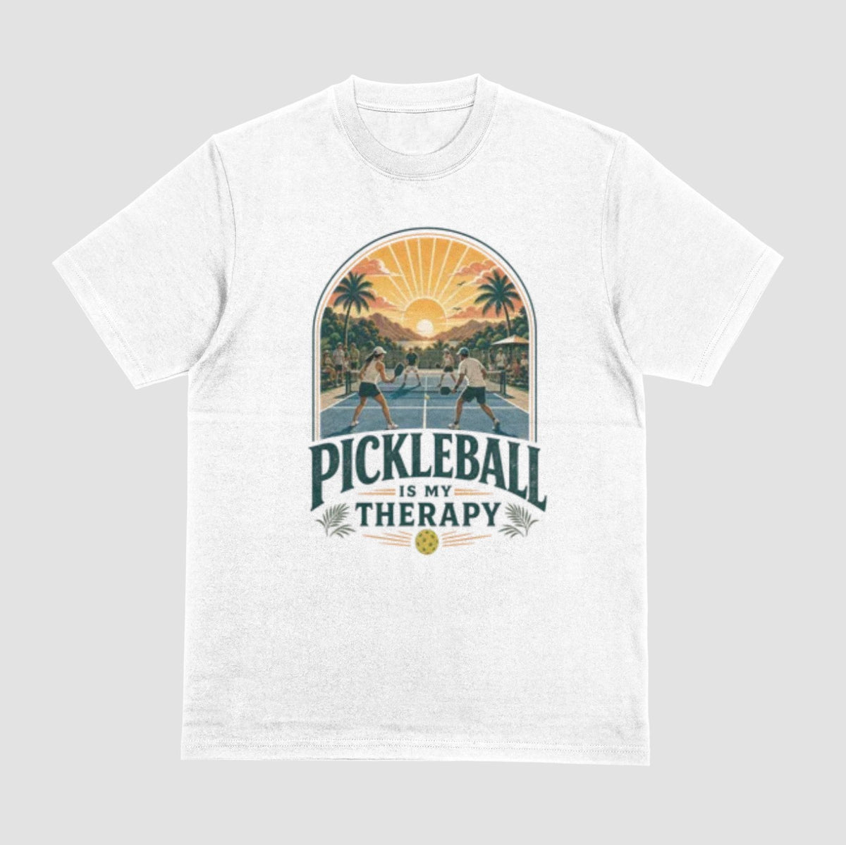 A white crewneck t-shirt featuring a retro-style graphic of pickleball players on a court with a sunset and palm trees, and the text 'PICKLEBALL IS MY THERAPY' printed below.